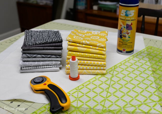 fabric, rotary cutter, and basting spray on cutting mat - supplies needed for QAYG tutorial