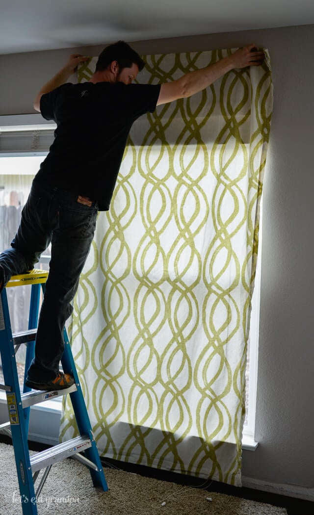 man standing on ladder to hang curtains