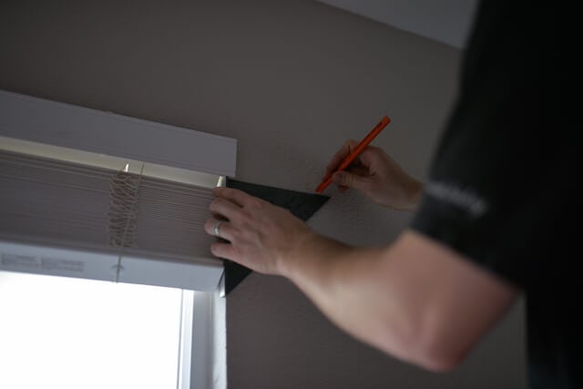 man measuring and marking spot with pencil where to hang curtains