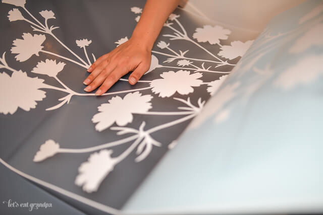 woman's hand placing floral decal on blue back of bookshelf