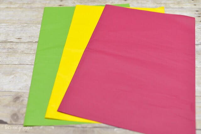green, yellow, and magenta tissue paper sheets fanned out on wooden background