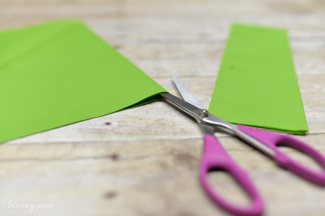 green tissue paper sheet on wooden background with corner cut off and scissors inserted in edge to cut