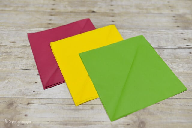 magenta, yellow, and green tissue paper sheet on wooden background, cut down to smaller squares