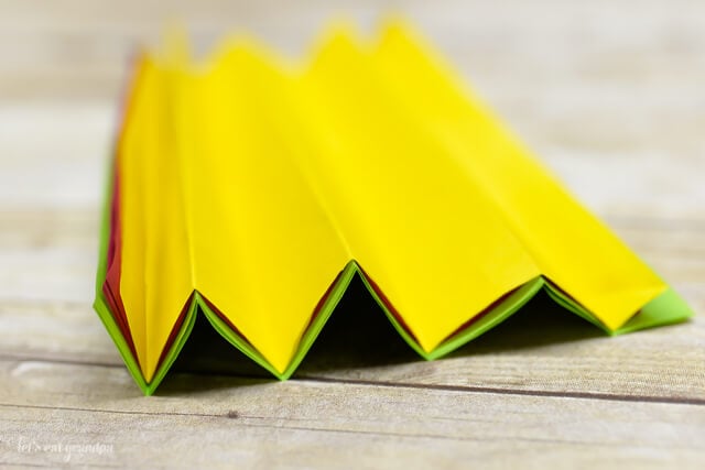magenta, yellow, and green tissue paper sheet stacked and folded accordion on wooden background