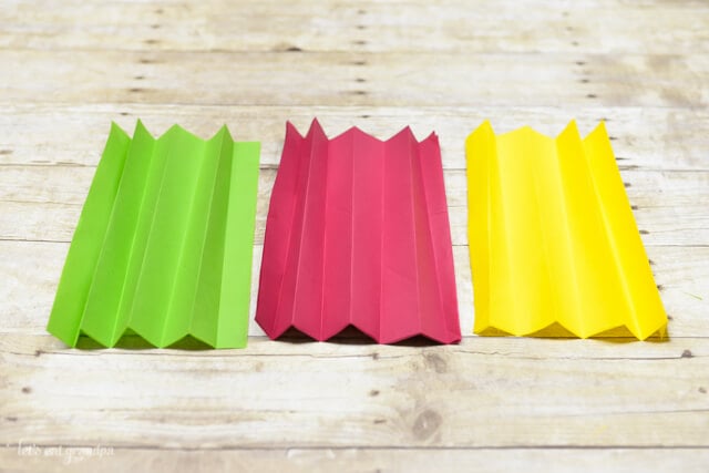 magenta, yellow, and green tissue paper sheet folded accordion style on wooden background
