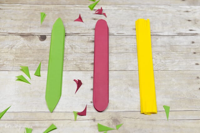 magenta, yellow, and green tissue paper folded in thin strips and edges trimmed on wooden background