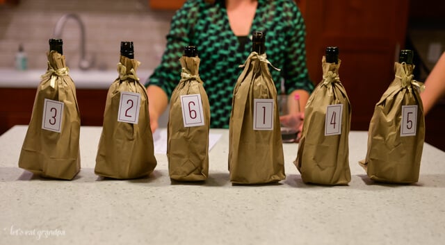 row of six red wines in brown bags with numbered labels on them