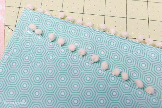 Fabric with pom poms attached to it lying on top of a green mat