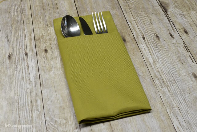 green napkin folded with a pocket and silverware inside