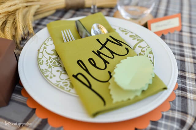 A place setting with two plates, two glasses, a name card and a napkin folded into a pocket holding a fork, knife and spoon