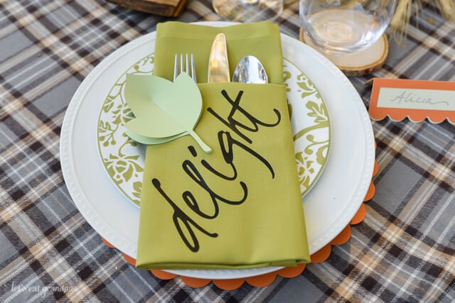 A place setting with two plates, two glasses, a name card and a napkin folded into a pocket holding a fork, knife and spoon