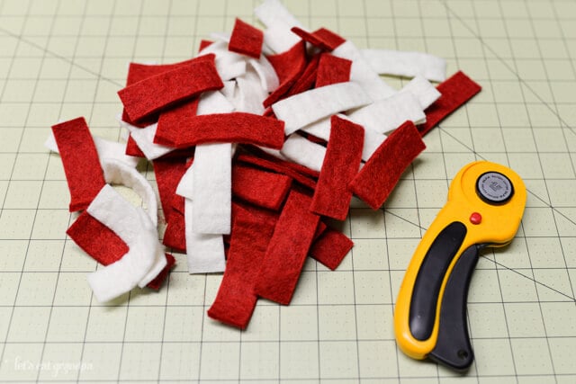 rotary cutter, cutting mat and strips of white and red felt cut 
